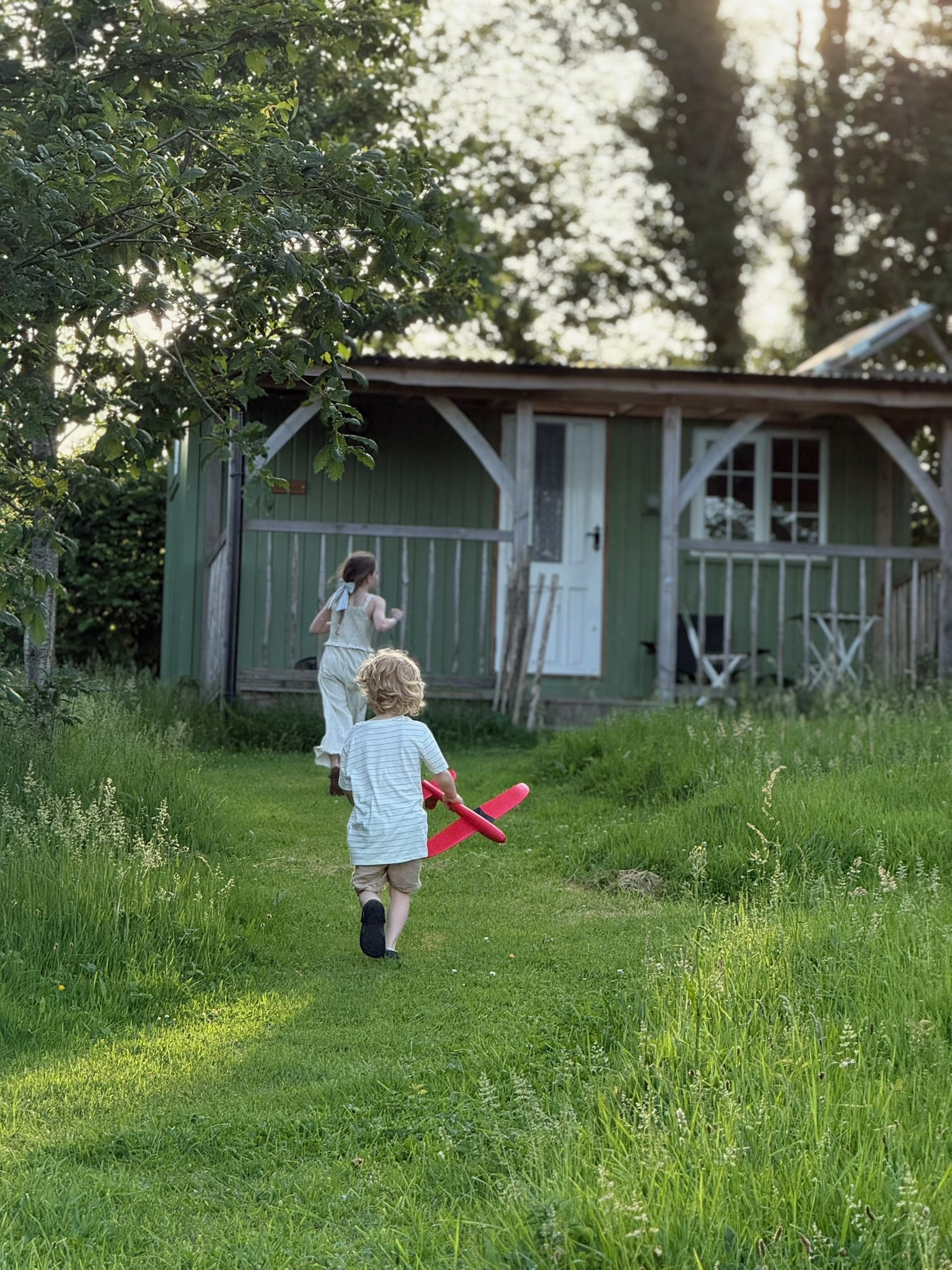 Shepherd's hut set in lush green woodland surrounded by trees with two children running towards the hut holding a red toy plane