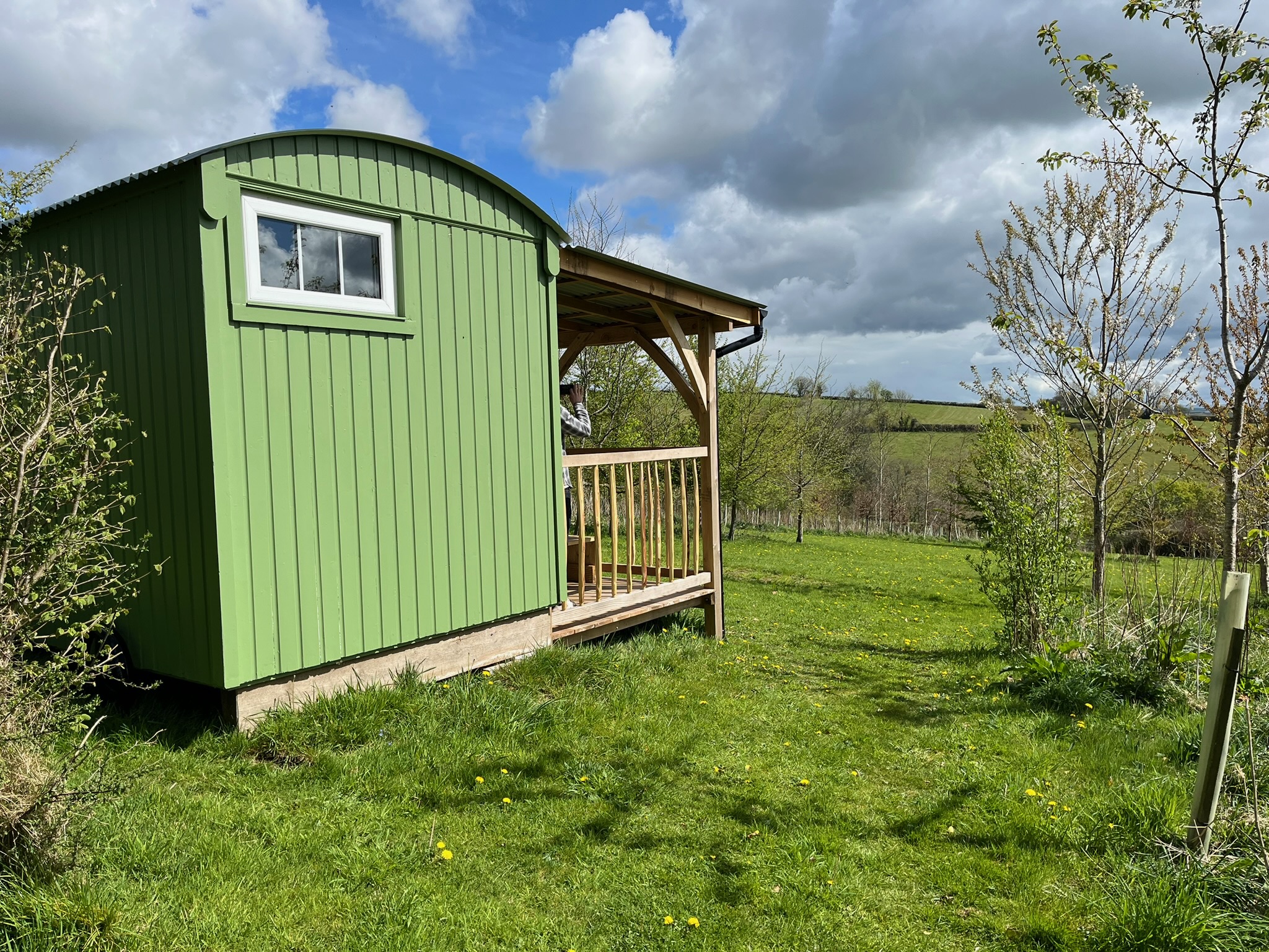 the side of a green shepherd's hut and the woodland surrounding it with the horizon in the distance