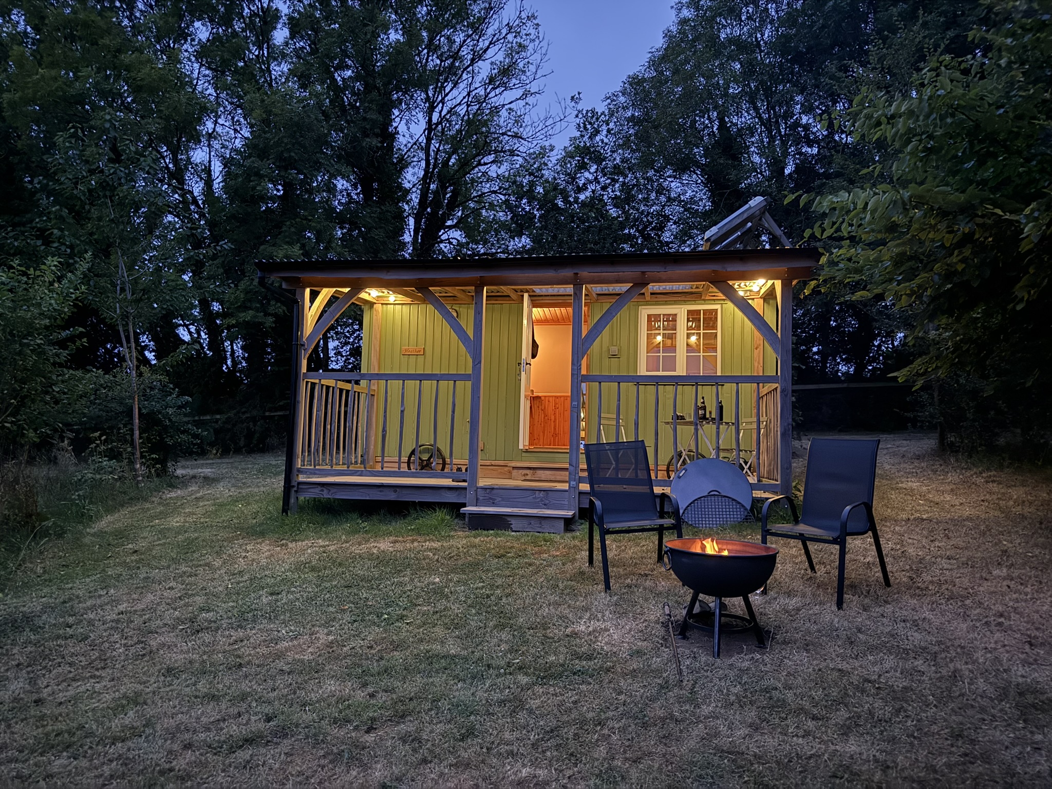 beautifully lit shepherd's hut with a lit fire pit and two chairs outside